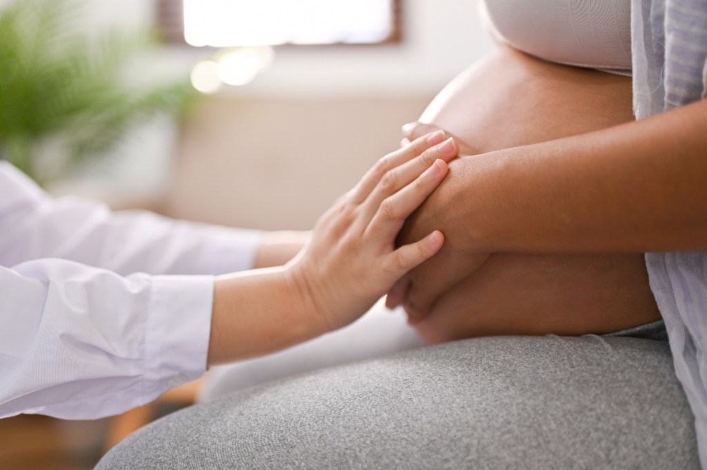 Doctor touches pregnant woman's stomach, showing importance of prenatal vitamins for maternal health